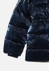 Manche d'une doudoune bleu foncé brillante avec un quilting horizontal et un poignet élastique sur fond blanc.