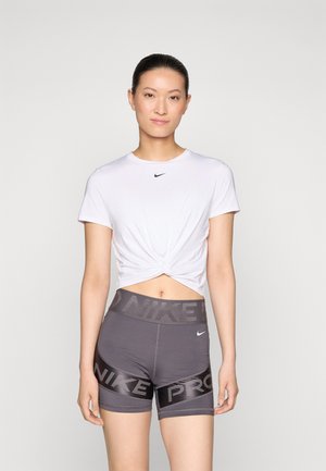 Biała krótka koszulka z przekręconym przodem i małym czarnym logo Nike, w połączeniu z szarymi szortami Nike Pro z szerokim pasem i akcentami logo.