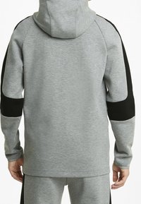 Sudadera gris con acentos negros en los hombros; tela suave y texturizada; cuenta con capucha y mangas largas; diseñada para un ajuste relajado.