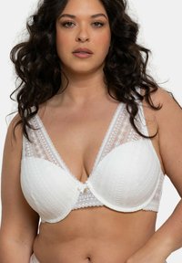 Soutien-gorge rembourré blanc avec une forme triangulaire, bordé de dentelle et orné de motifs géométriques. Dispose de bretelles réglables et d'un détail en forme de nœud au centre.