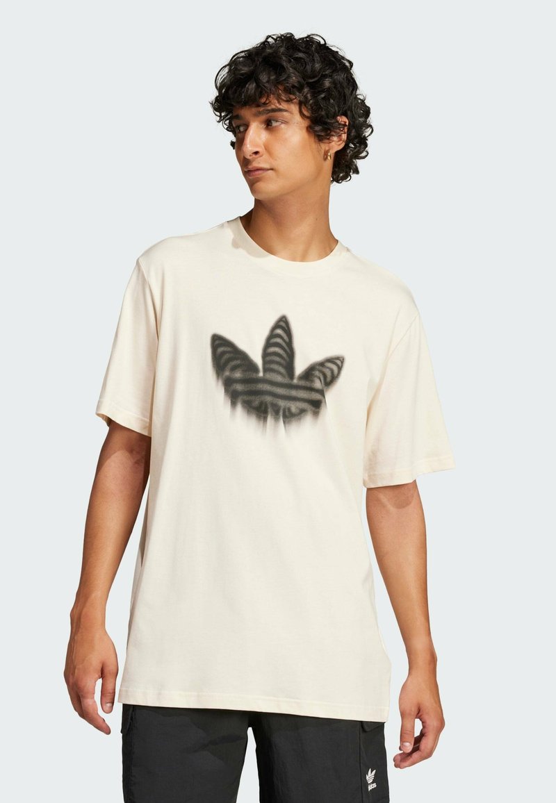 T-shirt in cotone beige chiaro con una grafica a gradiente nero e grigio che rappresenta tre forme simili a foglie sul petto. Vestibilità rilassata, maniche corte.