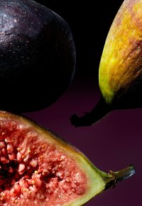 Svarta och gröna fikon, varav ett är skuret för att visa ett rosa fröigt inre. Skalets yta är slät och något glansig, mot en mörk bakgrund.