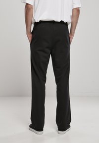 Sorte sweatpants med en afslappet pasform, elastisk talje og sidelommer, lavet af blødt stof; parret med grå slip-on sko.