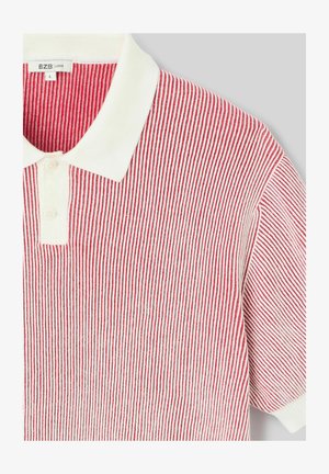 Polo à rayures verticales rouges et blanches, avec un col blanc et deux boutons sur la patte de boutonnage, étiqueté taille large.