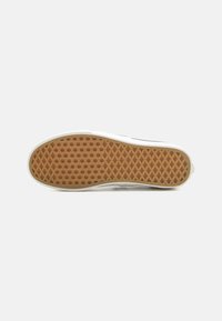 Fehér sneaker talp, amelyen egy méhsejt mintázatú, textúrált barna gumiszövés található. Az élek simák és enyhén kiemelkednek.