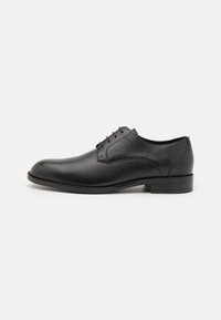 Chaussure habillée en cuir noir avec une texture lisse, bout arrondi, fermeture à lacets à cinq œillets et un petit talon empilé. Semelle avec un motif d'adhérence minimal.