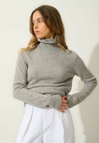 Maglione grigio a collo alto a maglia con una vestibilità comoda, colletto a coste e maniche lunghe, abbinato a pantaloni bianchi.