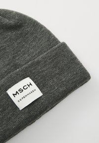 Grå strikket beanie med en foldet kant, som har et rektangulært hvidt mærke med sort tekst, der siger "MSCH COPENHAGEN." Blød tekstur.