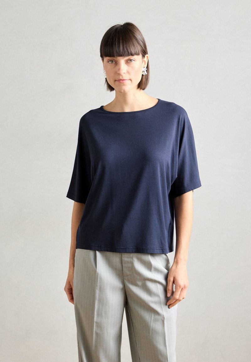 Top blu navy a maniche corte, colletto a giro, texture liscia, abbinato a pantaloni grigi chiari a righe, progettato per una vestibilità comoda.