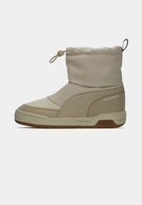 Beige waterdichte laars met een zachte textuur, ronde neus, elastische cuffsluiting en rubberen zool met een ingedrukte merklogo aan de achterkant.