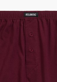 Burgundowe bawełniane szorty z elastycznym pasem, dwoma guzikami oraz kieszenią naszywaną z subtelnym detalem ściegów. Metka markowa mówi "ATLANTIC".
