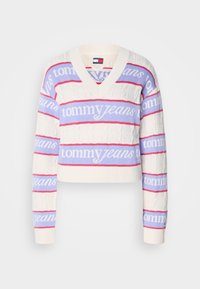 Witte gebreide trui met V-hals, versierd met horizontale roze en lichtblauwe strepen met de tekst "tommy jeans". Verkort model, textuurstof.