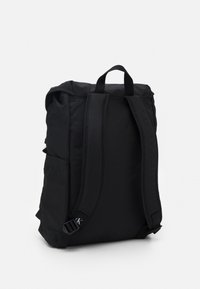 Mochila negra con correas de hombro acolchadas, bolsillos laterales y asa de transporte en la parte superior sobre un fondo blanco liso.