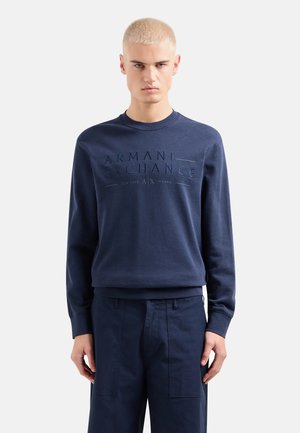 Felpa blu navy con logo "Armani Exchange" impresso, scollatura a girocollo e polsini a costine. Abbinata a pantaloni navy coordinati.