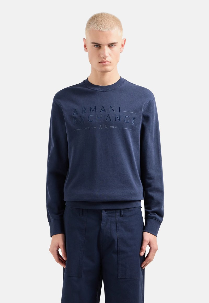 Felpa blu navy con logo "Armani Exchange" impresso, scollatura a girocollo e polsini a costine. Abbinata a pantaloni navy coordinati.