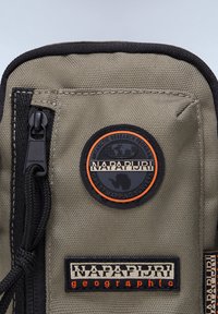 Olive green fabric pouch featuring a black zipper, textured surface, and circular logo with orange accents labeled "NAPAPIJRI" and "Antarctic Research Program."