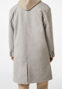 Hellgrauer Wollmantel mit Kapuze, geradem Schnitt, weiten Ärmeln und Knopfdetails an den Bündchen. Glatte Textur und minimalistisches Design.