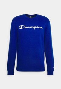 Modrá mikina vyrobená z měkké látky s bílým logem "Champion" na hrudi a žebrovanými manžetami a lemem.