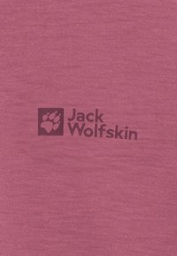 Dunkellila Jack Wolfskin-Logo mit Pfotenabdruck auf strukturiertem pinken Stoffhintergrund, zentriert.