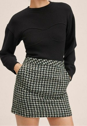 Czarny, prążkowany sweter z teksturowanym wzorem na dekolcie, połączony z krótką spódniczką we wzór houndstooth w czerni, bieli i odcieniach zieleni.