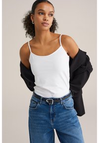 Fehér ujjatlan felső, kék, magas derekú farmernadrág fekete övvel és ezüst csattal, fekete dzseki, amely a vállakon lóg.