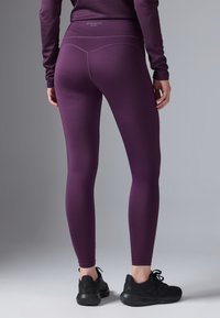 Leggings activos morados con cintura alta, textura suave y costuras planas, combinados con zapatillas deportivas negras.