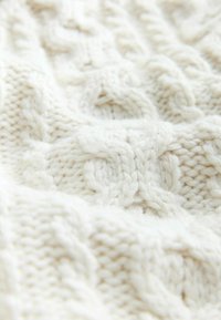 Adīta krēma krāsas džemperis ar stiegru rakstu, kuram ir bieza, teksturēta šuvuma struktūra. Audumam ir mīksta, pūkaina izskats ar paceltiem rakstiem.