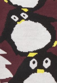 Stickad tyg med ett upprepat mönster av pingviner. Pingvinerna är svarta med vita magar och gula detaljer, på en burgundy bakgrund.