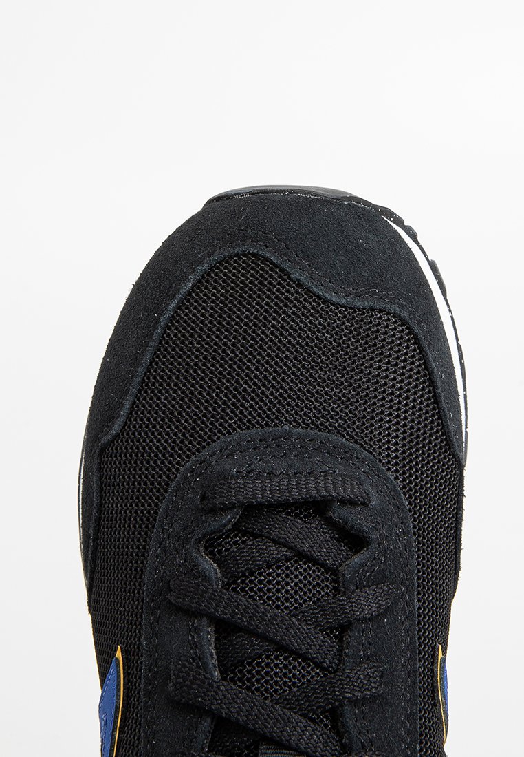 Zapatilla negra con parte superior de tejido de malla, superposiciones de ante, cordones negros y pequeños detalles en azul y amarillo cerca de la suela.