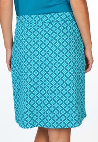 Ein türkisfarbener Rock mit einem geometrischen Muster aus abwechselnden Rauten und Kreisen, gefertigt aus einem strukturierten Stoff mit einem glatten Bund.