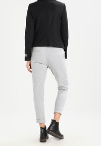 Svart figursydd jacka med silverrandiga detaljer, i kombination med ljusgrå tajta sweatpants och svarta ankelstövlar med texturerad sula.