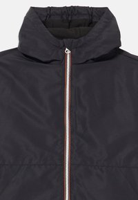 Veste bleu marine foncé avec un col haut, une fermeture éclair centrale blanche avec des accents rouges et une texture lisse et mate. Pas de motifs visibles.