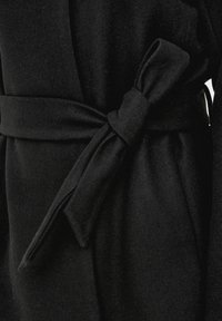 Manteau en laine noire noué autour de la taille avec une large ceinture en tissu fermement attachée.