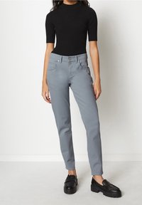 Pantalones grises de corte slim y diseño de cinco bolsillos, combinados con una blusa negra de manga corta y unos loafers gruesos negros. Textura suave, aspecto casual.