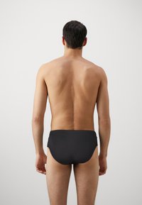 Schwarze Schwimmbriefs aus dehnbarem Material. Einfaches Design mit glatter Textur, keine sichtbaren Akzente oder Muster. Saubere Linien.