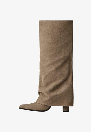 Visoka bež čizma od brušene kože s uskim vrhom, strukturiranim oblikom i blok petom. Ima glatku teksturu i minimalistički dizajn.