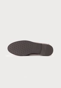 Suela de zapato de goma marrón con un patrón texturizado de pequeñas letras. Forma redondeada con un ligero tacón y bordes suaves.