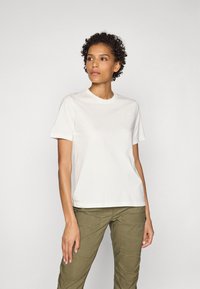 Cremfarvet bomulds t-shirt med korte ærmer, rund halsudskæring og diskret branding på brystet, parret med olivengrønne cargobukser.