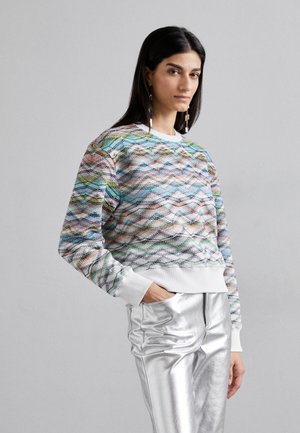 Multicolored sweater with a wave pattern, round neckline, and white cuffs paired with shiny silver trousers.