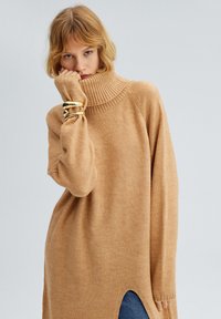 Kamel turtleneck sweater med en afslappet pasform, ribbet krave og sideskår. Blød tekstur, lange ærmer og en subtil glans.