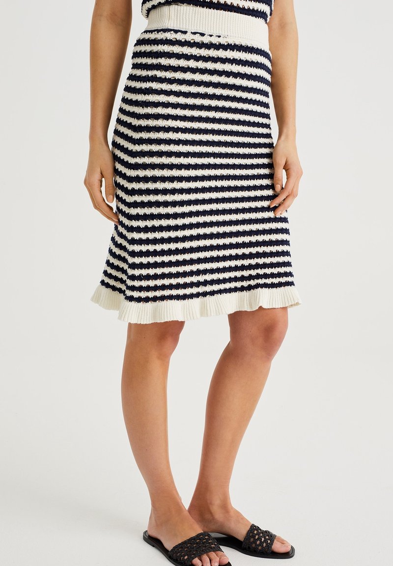 Stickad kjol med mörkblå och krämfärgade horisontella ränder, en ribbad midja och en volangnert. Bärs med svarta sandaletter.