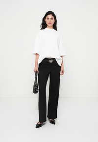 Λευκό υπερμεγέθες t-shirt, μαύρο παντελόνι ραμμένο με κουστούμι, ασημένια αγκράφα ζώνης σε σχήμα καρδιάς, μαύρα μυτερά παπούτσια και τσάντα με πουά στο χέρι.