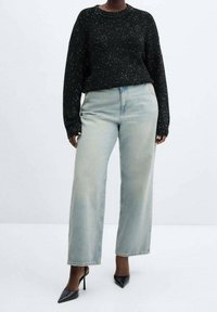 Czarny sweter o błyszczącej strukturze, zestawiony z jasnoniebieskimi spodniami o szerokich nogawkach i czarnymi szpilkami. Prosty, codzienny strój.