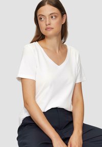 T-shirt en coton blanc avec un décolleté en V et des manches courtes. Présente une coupe décontractée et une texture douce, associée à un pantalon sombre.