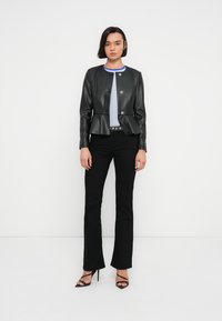 Μαύρο δερμάτινο μπουφάν με σχέδιο πεπλούμ, ασημί κουμπιά με πατητήρι, φορεμένο πάνω από ριγέ πουκάμισο, συνδυασμένο με στενά μαύρα παντελόνια και πέδιλα με λουριά.