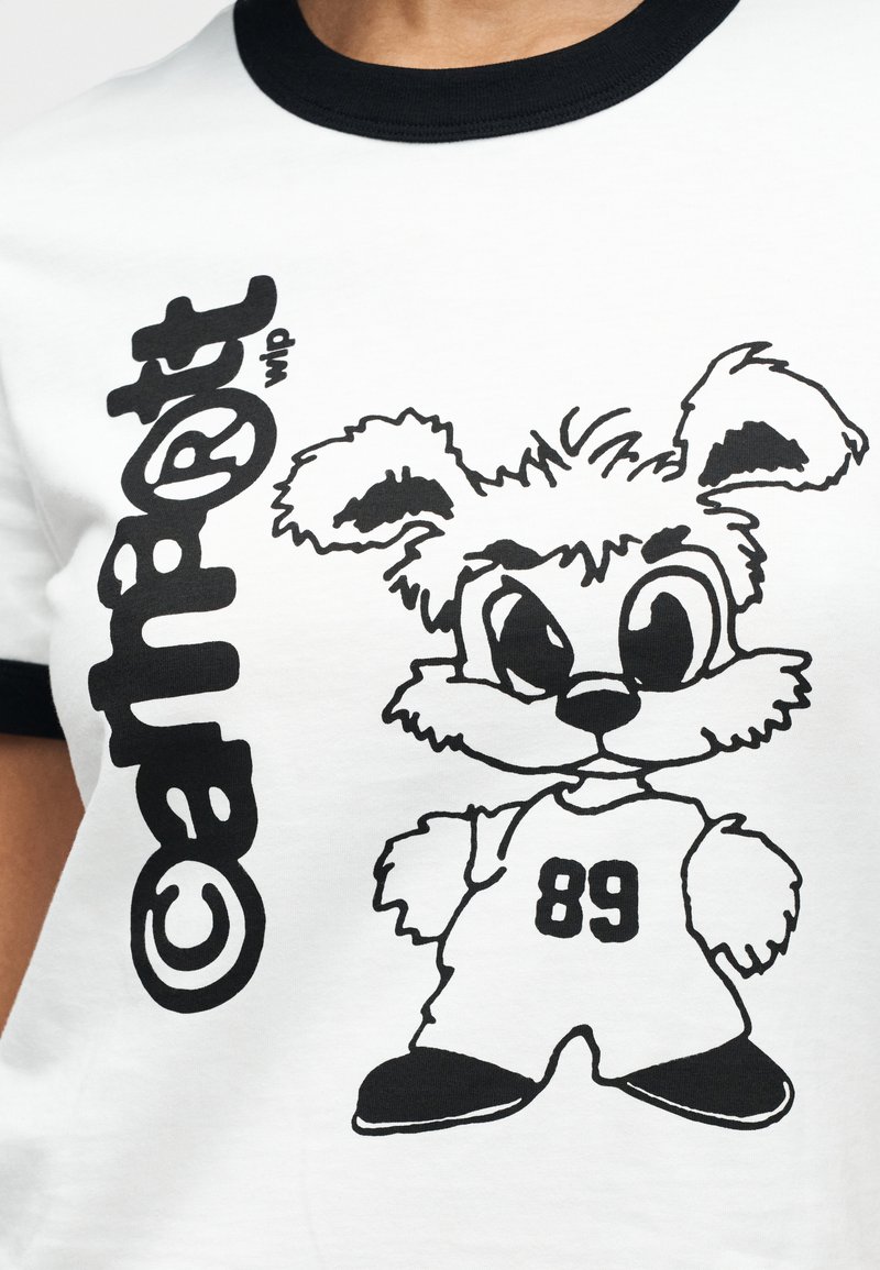 Maglietta bianca con bordo nero che presenta un coniglio dei cartoni animati con caratteristiche esagerate, indossando una maglia con il numero '89'. Il design è audace e grafico.