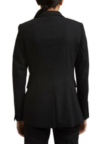 Czarna marynarka o dopasowanym kroju z wyraźnymi ramionami, z jedną rozcięciem z tyłu i teksturowanym materiałem. Posiada standardowe klapy i dopasowaną sylwetkę.