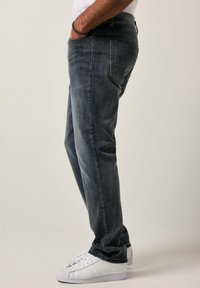 Jeans de mezclilla en un lavado gris oscuro, con un diseño de pierna recta, cinco bolsillos y sutiles detalles de costura, combinados con zapatillas blancas.