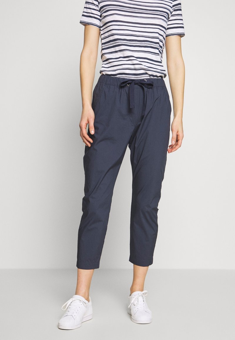 Pantalon court bleu marine avec taille élastique et cordon de serrage ajustable, associé à un t-shirt à manches courtes rayé et des baskets blanches.
