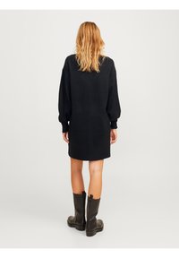 Abito nero a maglia con maniche lunghe, polsini a costine e orlo. Tessuto liscio, lunghezza media, abbinato a stivali neri alti fino al ginocchio.